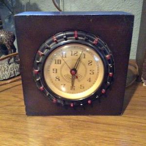 May include: A vintage wooden clock with a black face and red accents. The clock face has white numbers and hands. The clock is in a dark wood frame.
