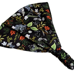 May include: A black headband with an all-over floral pattern. The design features green leaves, white flowers, and orange accents. The headband has an elasticated section for a comfortable fit.
