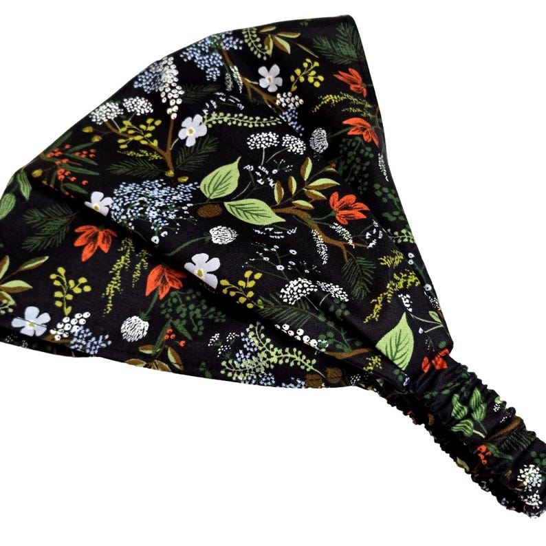 May include: A black headband with an all-over floral pattern. The design features green leaves, white flowers, and orange accents. The headband has an elasticated section for a comfortable fit.