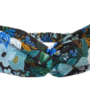 May include: A black headband with a floral pattern in shades of blue, green, and white. The headband is made of a soft, stretchy fabric and is designed to be worn as a twisted knot.
