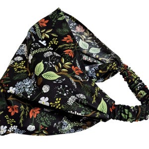 May include: A black headband with an all-over floral pattern. The design features green leaves, white flowers, and orange accents. The elastic band is black with a matching floral print.