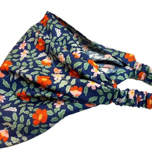 May include: A blue floral headband with a stretchy elastic band. The headband features a repeating pattern of pink and orange flowers, green leaves, and white butterflies.