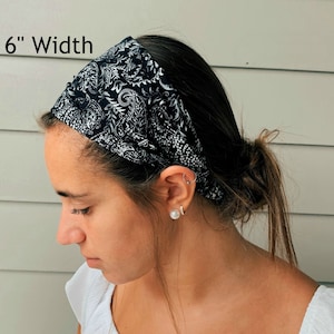 May include: A black and white paisley patterned headband, 6 inches wide, worn across the forehead. The fabric design features a detailed floral and leaf pattern. The headband is made of a soft, flexible material.
