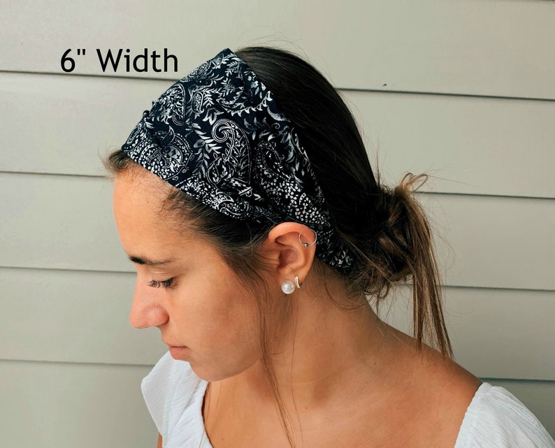 May include: A black and white paisley patterned headband, 6 inches wide, worn across the forehead. The fabric design features a detailed floral and leaf pattern. The headband is made of a soft, flexible material.