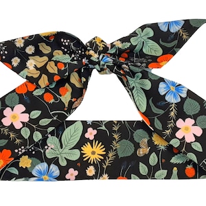May include: A black headband with a floral print featuring red, orange, pink, blue, yellow, and green flowers. The headband is tied in a bow.