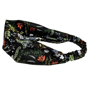 May include: A black headband with an elastic back and a floral pattern. The pattern includes orange, white, and green flowers and foliage. The headband is designed to be worn around the head.