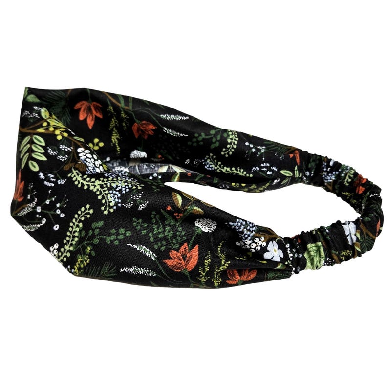 May include: A black headband with an elastic back and a floral pattern. The pattern includes orange, white, and green flowers and foliage. The headband is designed to be worn around the head.