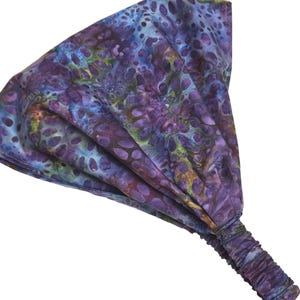 May include: A wide headband with an abstract pattern in shades of purple, blue, and green. The fabric has a textured appearance with a repeating pattern of organic shapes. The elasticated section is visible at the back.