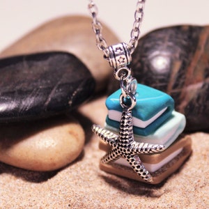 Op de afbeelding: Een zilveren ketting met een bedel met een stapel kleurrijke, strandthema-tegels en een zilveren zeester.