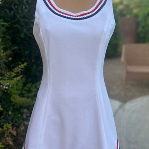 May include: White sleeveless tennis dress with red, white, and blue trim around the neckline and hem.