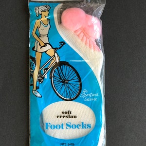 May include: A pack of white soft creslan foot socks with a pink pom-pom on top. The pack has a blue background with a woman riding a bicycle and the text "soft creslan Foot Socks" and "for Sportand Leisure".