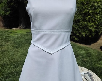 May include: A light blue sleeveless dress with a round neckline and a fitted waist. The dress features a decorative V-shaped detail at the waist and a scalloped lace hemline. The dress is displayed on a mannequin outdoors.