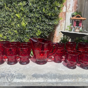 Op de afbeelding: Een set van 12 rode glazen bekers en een bijpassende kan. De glazen en de kan hebben een getextureerd, ruitvormig patroon.