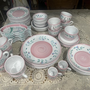 以下が含まれることがあります： ピンクと白の花柄のセラミック製の食器とカップのセット。セットには、プレート、ボウル、ソーサー、ティーカップが含まれています。