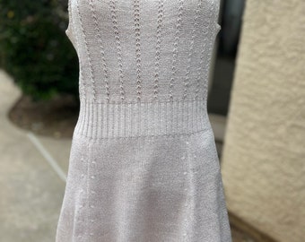 May include: A white sleeveless knit dress with a scoop neck and a fitted bodice. The dress has a flared skirt and a delicate openwork pattern.