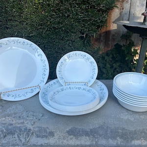 May include: A set of white Corelle dinnerware with a blue and green floral pattern. The set includes a large dinner plate, a salad plate, a bowl, and a set of smaller bowls.