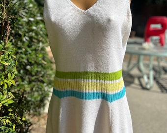 May include: White sleeveless knitted dress with a v-neck and a colorful striped band around the waist.