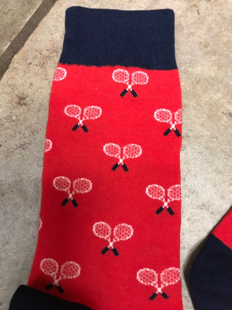 May include: Red socks with a navy blue cuff and toe. The socks feature a pattern of white tennis rackets. The socks are made of a soft, comfortable material.