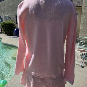 May include: A light pink knit sweater and skirt set. The sweater has long sleeves and a white trim around the collar and cuffs. The skirt has a decorative openwork pattern around the hem.