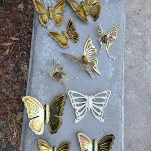 May include: A selection of metal butterfly sculptures in various sizes and styles. The butterflies feature gold, white, and iridescent finishes. Some have detailed wing designs, while others have a more minimalist aesthetic.