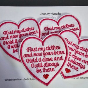 Op de afbeelding: Vijf rode hartvormige viltpatches met witte borduursels. De tekst op de patches luidt "First my clothes and now your bear. Hold it close and I will always be there."