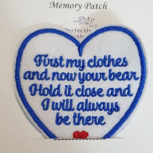 Op de afbeelding: Witte hartvormige viltpatch met blauwe geborduurde rand. De patch heeft de tekst "First my clothes and now your bear Hold it close and I will always be there" in blauwe borduurwerk. Een klein rood hart is onderaan de patch geborduurd.