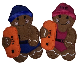 May include: Two felt gingerbread people, one in a blue swim cap and trunks, the other in a pink swim cap and swimsuit. Each holds an orange float with the word "safe". The pink cap has the name "Fran".