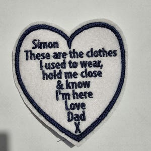 May include: A heart-shaped patch with a white felt center and a navy blue stitched border. The patch features embroidered text that reads "Simon, These are the clothes I used to wear, hold me close & know I'm here Love Dad X."