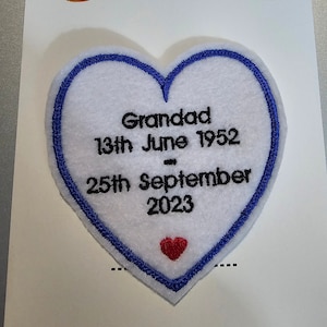 May include: A white heart-shaped memory patch with a blue border, featuring the text "Grandad 13th June 1952 - 25th September 2023" in black. A small red heart is at the bottom. The patch is on a white background.
