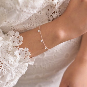 May include: A delicate silver chain bracelet with small, clear crystal charms dangling from it.