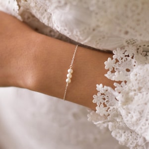 Peut inclure: Un bracelet délicat en chaîne argent avec trois petites perles blanches.