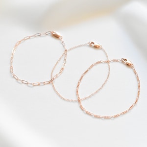 Puede incluir: Tres pulseras de cadena dorada sobre un fondo blanco. Las pulseras est&aacute;n hechas de cadenas delicadas y enlazadas.