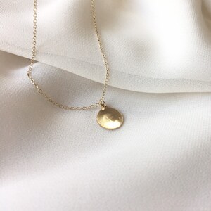 May include: A delicate gold chain necklace with a small, round, hammered gold pendant.