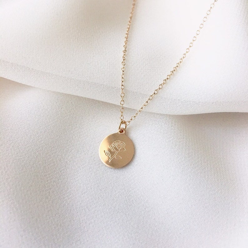May include: A gold chain necklace with a round pendant featuring a delicate rose design.