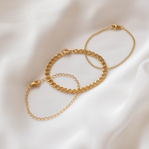 May include: Three gold chain bracelets, one with a thick curb chain, one with a delicate chain, and one with a thin chain. The bracelets are on a white background.