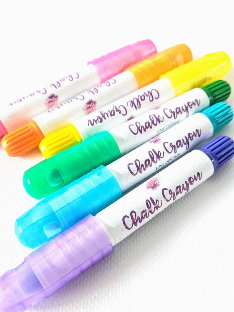 May include: Six colorful chalk crayons with a white label that says "Chalk Crayon Love Designs". The crayons are in the colors pink, yellow, green, blue, and purple.