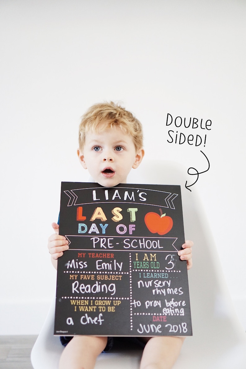 May include: A black chalkboard sign with colorful text that reads "Liam's Last Day of Pre-School". The sign has a red apple graphic and includes information about Liam's teacher, age, favorite subject, and what he wants to be when he grows up. The sign is dated June 2018.