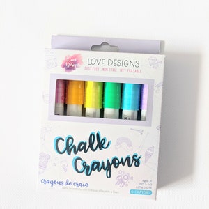 May include: A box of six colorful chalk crayons. The box features the words "Chalk Crayons" in a playful font, with the brand name "Love Designs" at the top. The crayons are visible through a clear window, showcasing a rainbow of colors.
