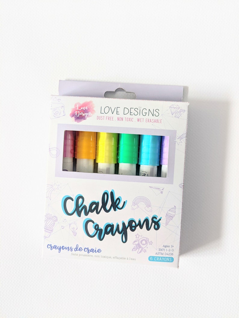 May include: A box of six colorful chalk crayons. The box features the words "Chalk Crayons" in a playful font, with the brand name "Love Designs" at the top. The crayons are visible through a clear window, showcasing a rainbow of colors.