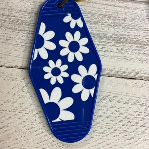 以下が含まれることがあります： 白いデイジー柄の青いプラスチック製モテルキータグ