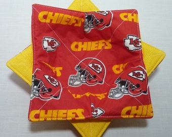 May include: A square, red bowl cozy with a yellow backing. The red fabric is patterned with football helmets and the word "CHIEFS" in yellow. The cozy is designed to hold a bowl and protect hands from heat.