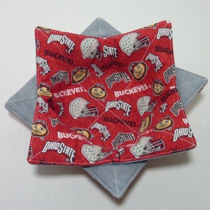May include: A red and gray bowl cozy with a quilted design. The red fabric is patterned with the words "OHIO STATE" and "BUCKEYES", along with images of helmets and a mascot. The cozy is designed to hold a bowl.