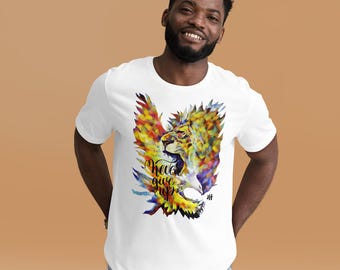 Op de afbeelding: Wit T-shirt met een kleurrijke afbeelding van een leeuw met adelaarsvleugels. Het ontwerp bevat de woorden "Never Give Up" in zwart schrift. Het kunstwerk bevat tinten geel, oranje, blauw en groen.