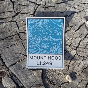 May include: A white sticker with a blue topographic map of Mount Hood. The sticker reads "Mount Hood 11,249'" in black text.