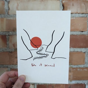 May include: A black and white illustration of a winding path leading through a canyon with a red sun setting in the distance. The text "Do it scared" is written below the image.
