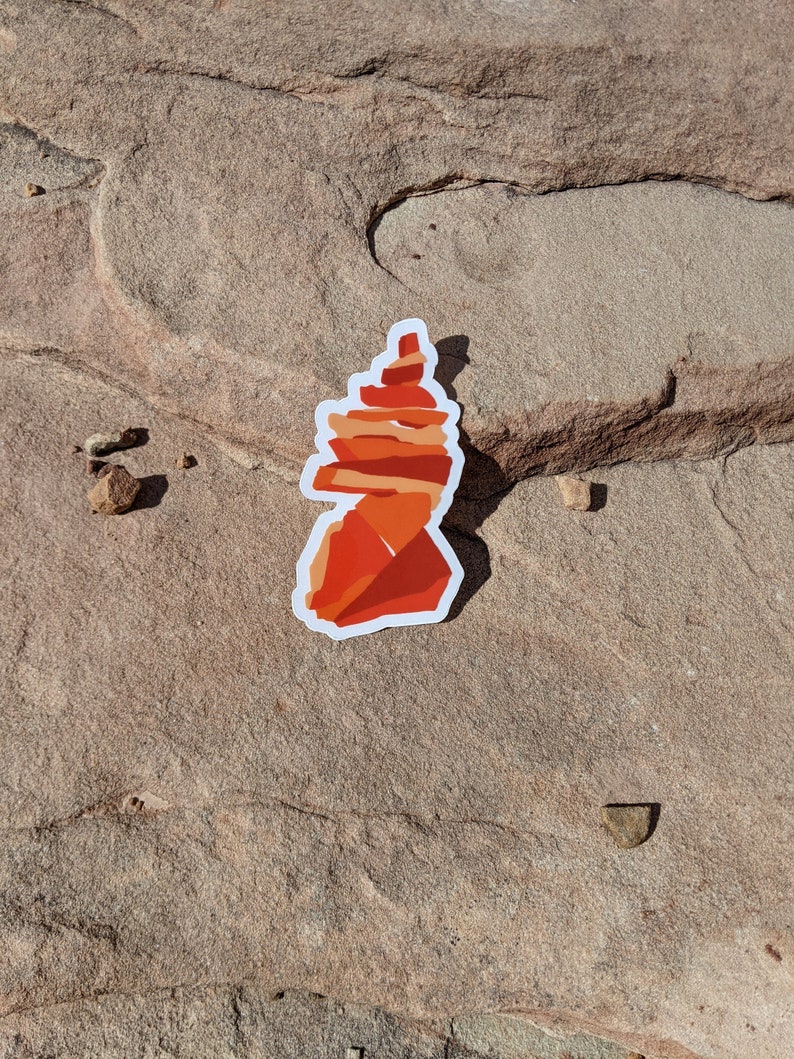 May include: A red and orange layered rock formation sticker. The sticker is on a brown, textured surface.