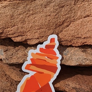 May include: A white sticker with an orange and red illustration of a rock formation. The rock formation is stacked in a spiral shape.
