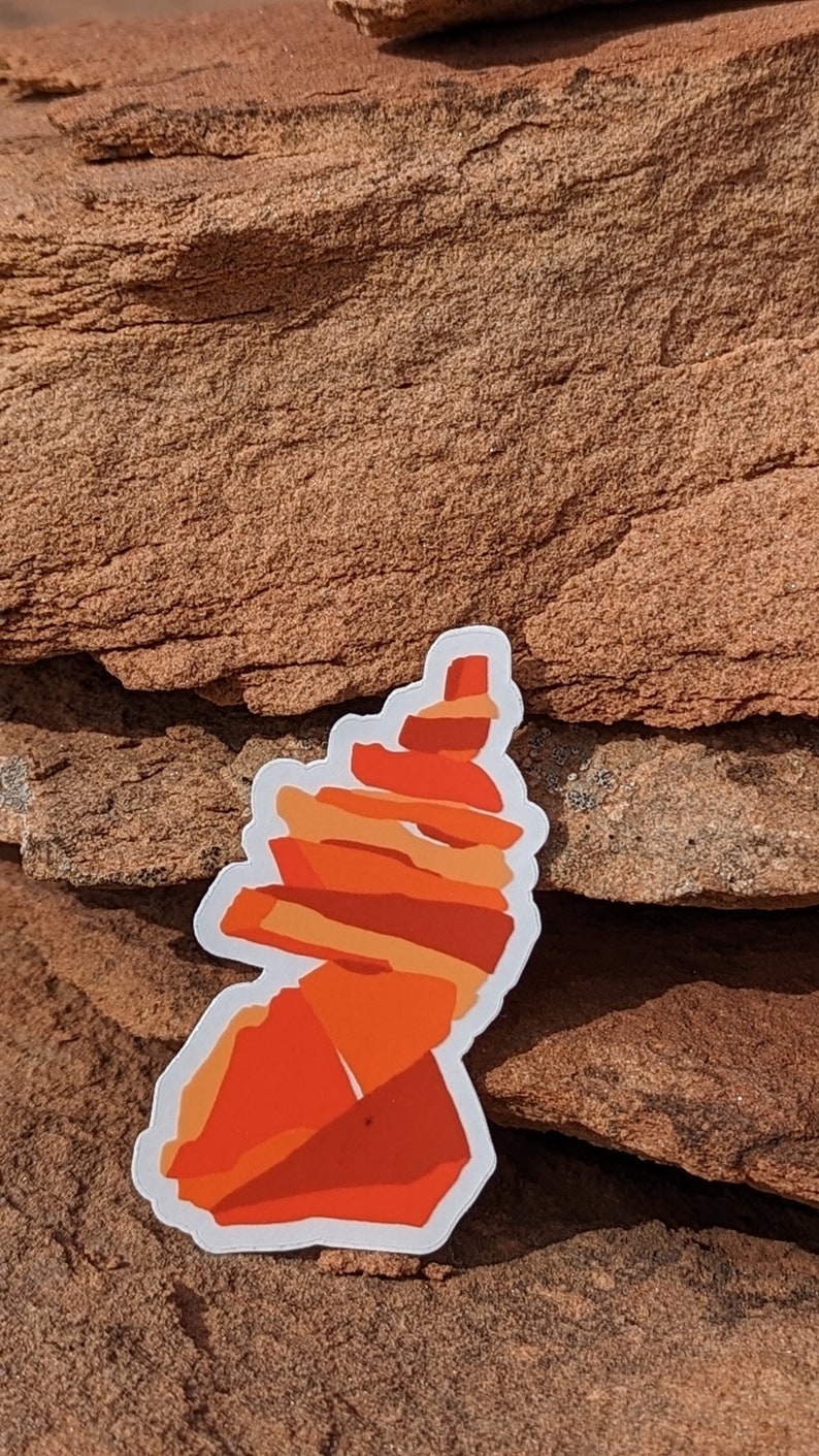 May include: A white sticker with an orange and red illustration of a rock formation. The rock formation is stacked in a spiral shape.