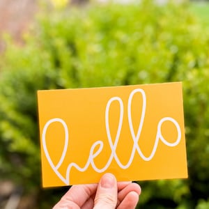 May include: A yellow card with the word "hello" written in white cursive.