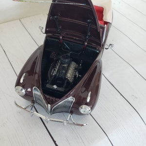 May include: A detailed model of a classic burgundy convertible car with the bonnet open, revealing the engine. The car has a cream-coloured top and chrome accents on the front bumper and grill. The interior is red.
